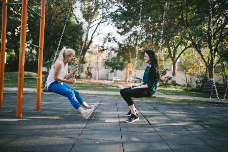 Two Teens Girls Sitting on Swings Talking to Each Other