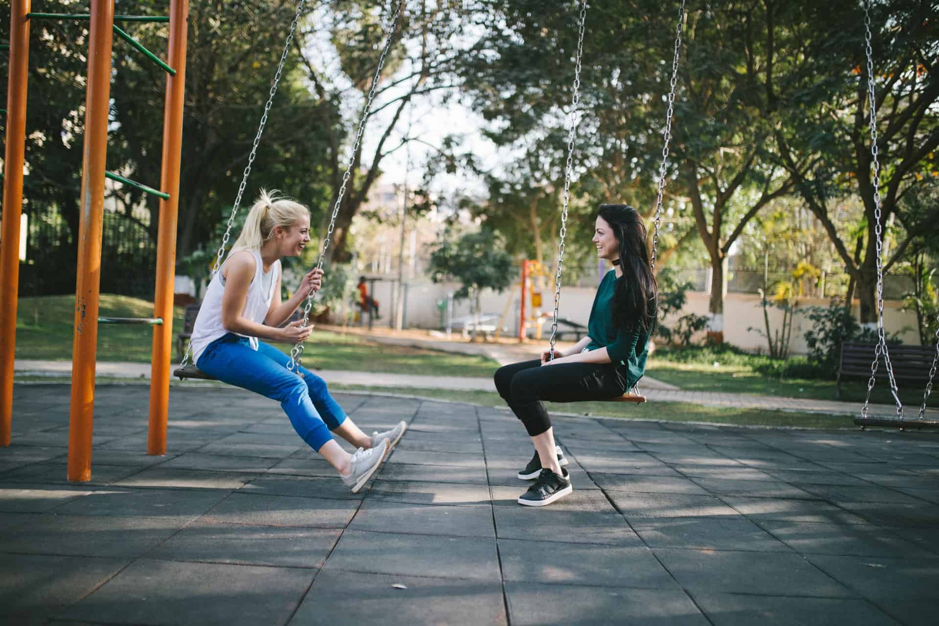 Two Teens Girls Sitting on Swings Talking to Each Other