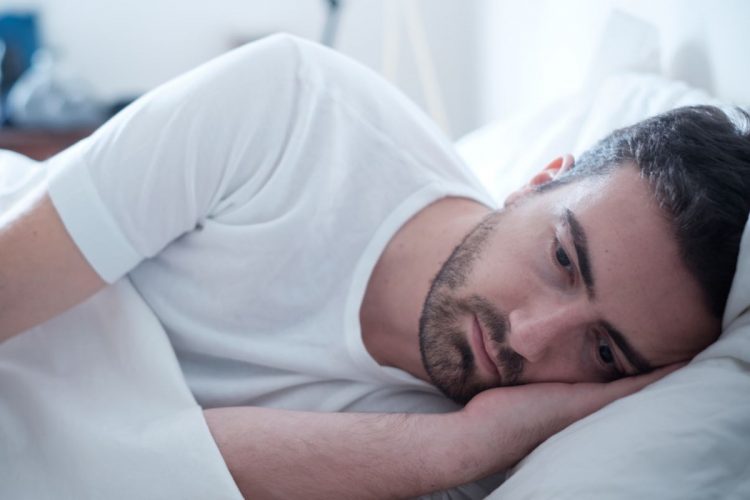A sad man lying in bed