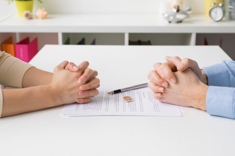A man and woman sit opposite each with documents and wedding rings on the table