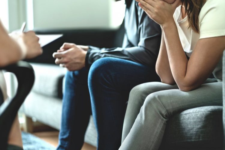 A couple sitting on the couch with a therapist looking unhappy