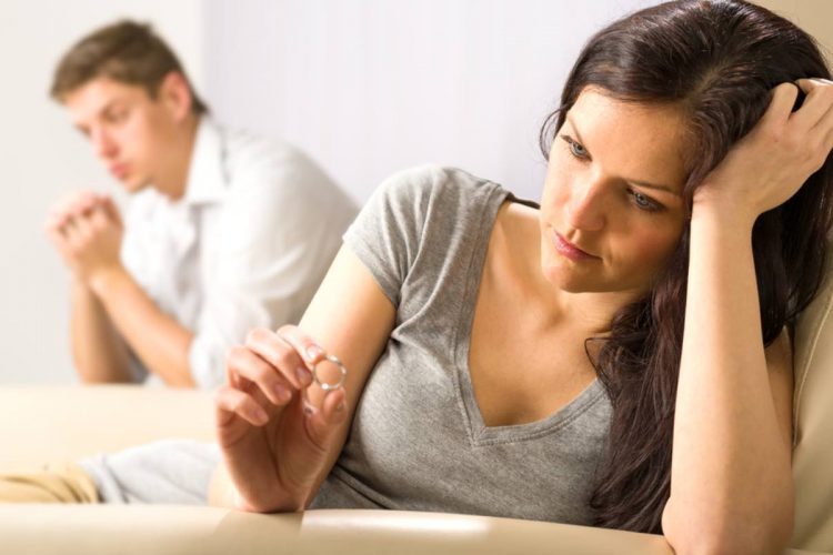 A woman sitting on the bed looking at her wedding ring