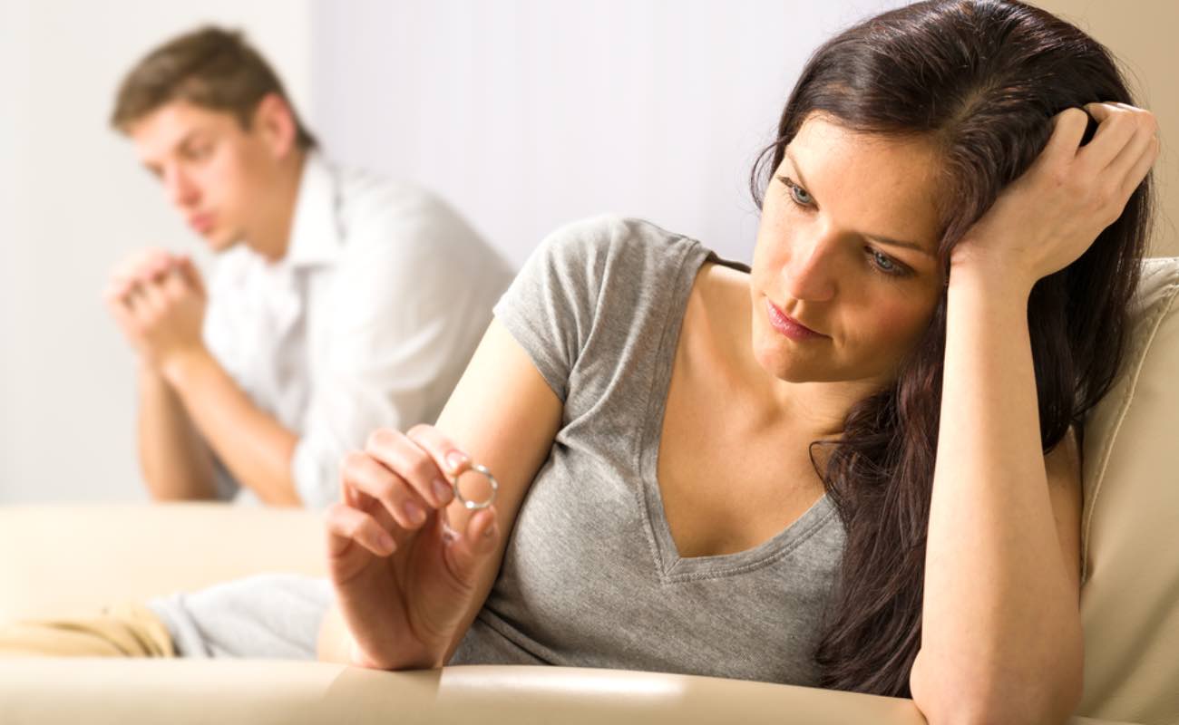 A woman sitting on the bed looking at her wedding ring