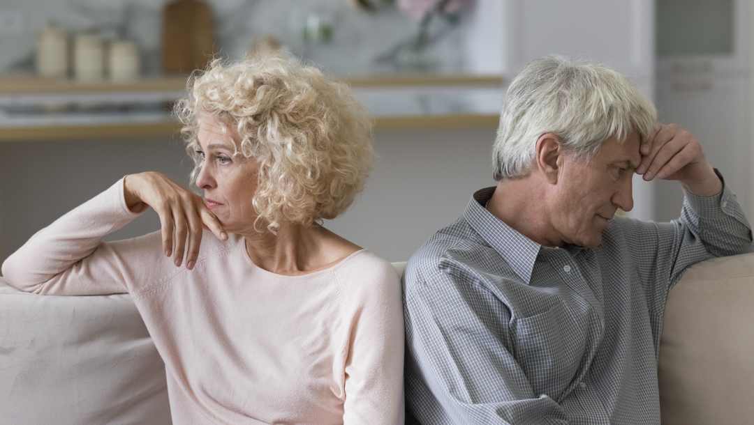 Two elderly people looking upset on either side of the couch to each other